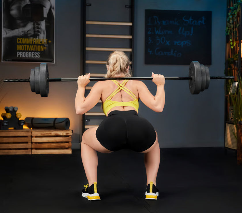 Person performing a barbell squat in a gym setting with motivational posters on the wall.